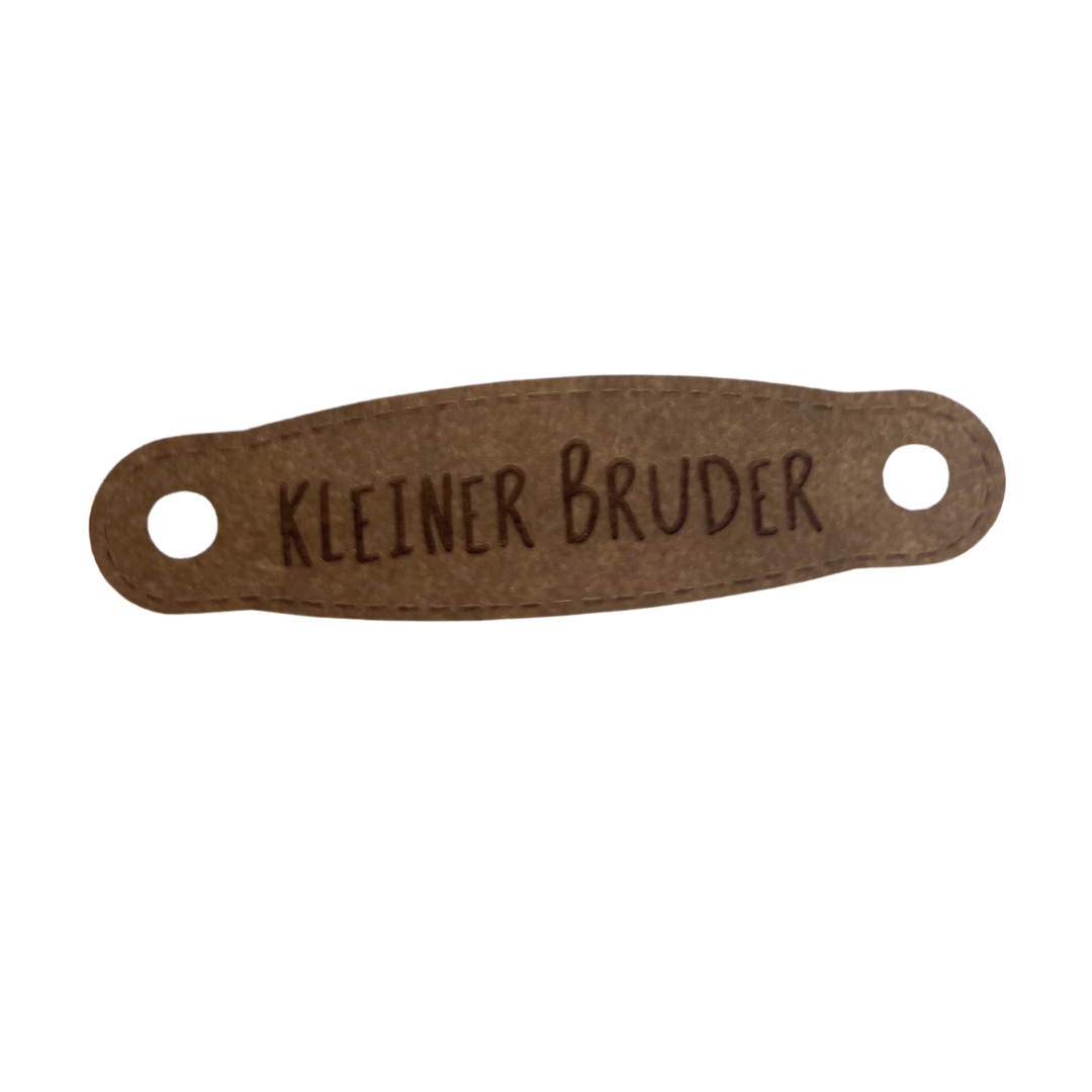 Hier ist das Etikett mit der Schrift "Kleiner Bruder" zu sehen. Es ist eine ovale Form mit zwei Löcher an der linken und rechten Seite.