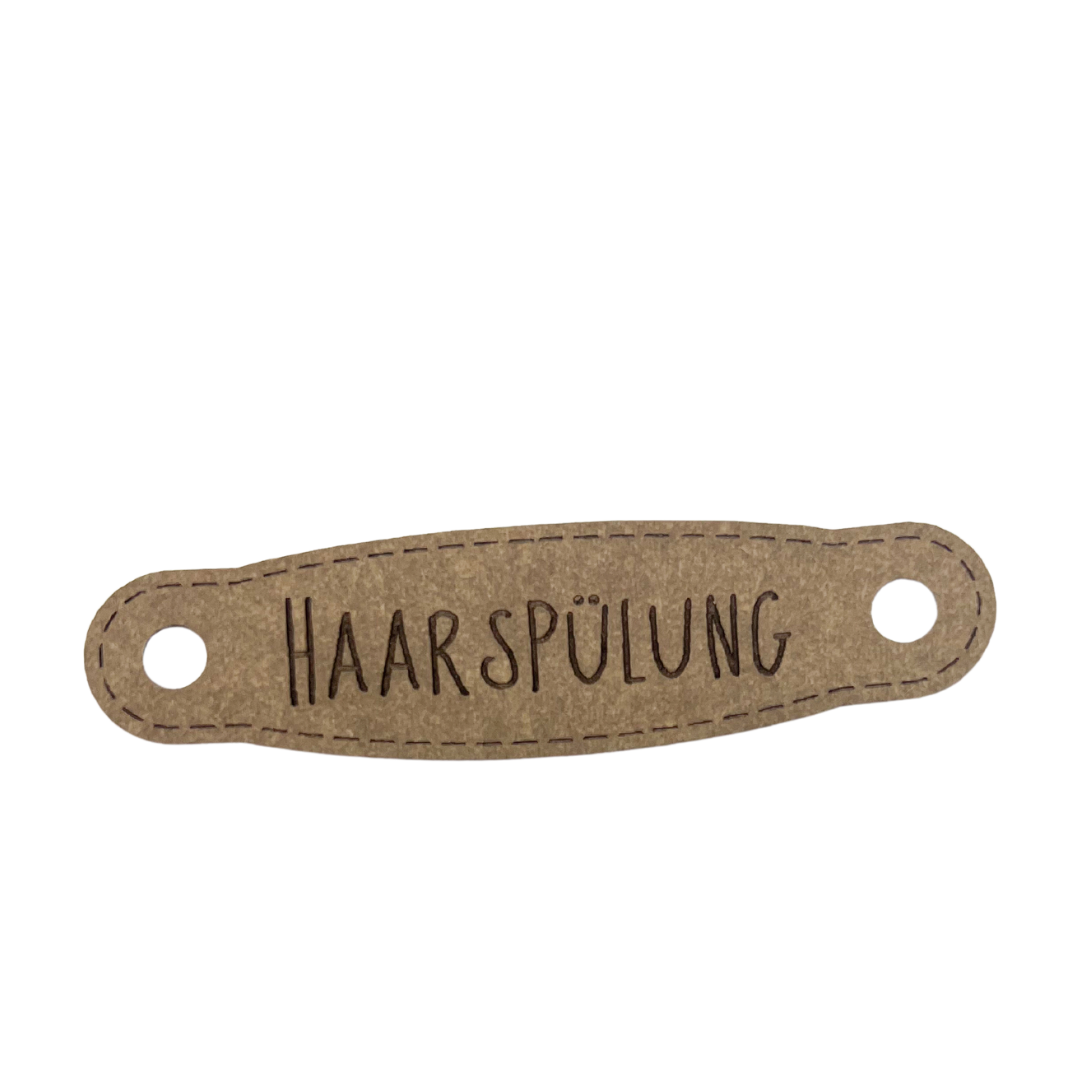 Hier ist das Etikett mit der Schrift "Handspülung" zu sehen. Es ist eine ovale Form mit zwei Löcher an der linken und rechten Seite.