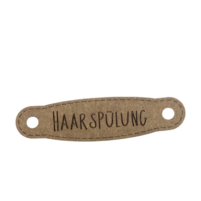 Hier ist das Etikett mit der Schrift "Handspülung" zu sehen. Es ist eine ovale Form mit zwei Löcher an der linken und rechten Seite.