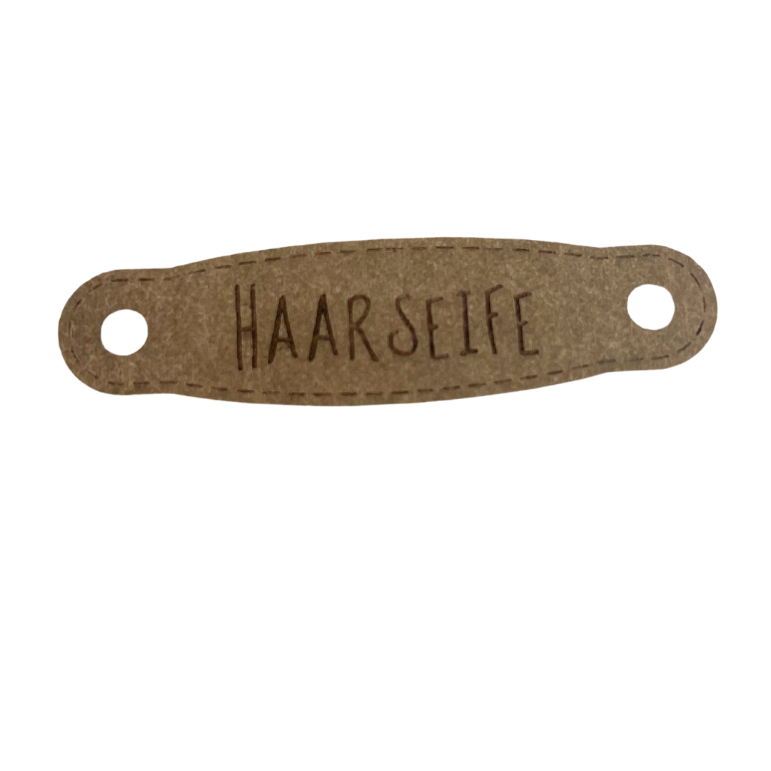 Hier ist das Etikett mit der Schrift "Haarseife" zu sehen. Es ist eine ovale Form mit zwei Löcher an der linken und rechten Seite.