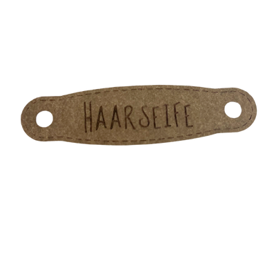Hier ist das Etikett mit der Schrift "Haarseife" zu sehen. Es ist eine ovale Form mit zwei Löcher an der linken und rechten Seite.