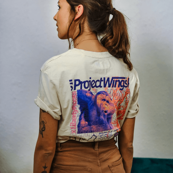 Eine Frau mit dem Rücken zugekehrt. Angezogen hat sie ein Urban T-Shirt in beige und eine braune Hose