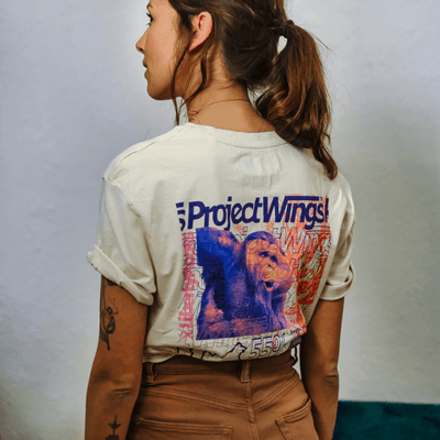 Eine Frau mit dem Rücken zugekehrt. Angezogen hat sie ein Urban T-Shirt in beige und eine braune Hose