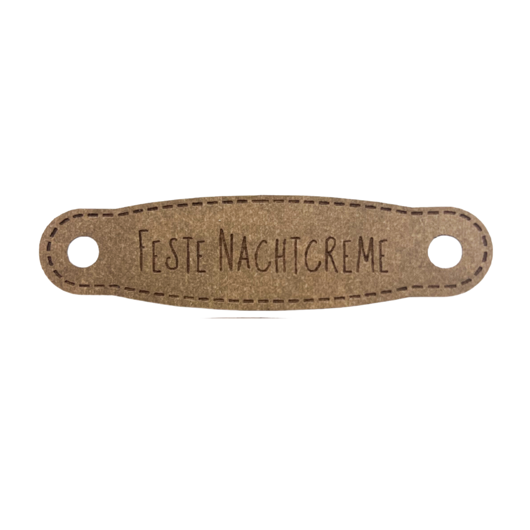 Hier ist das Etikett mit der Schrift "Feste Nachtcreme" zu sehen. Es ist eine ovale Form mit zwei Löcher an der linken und rechten Seite.